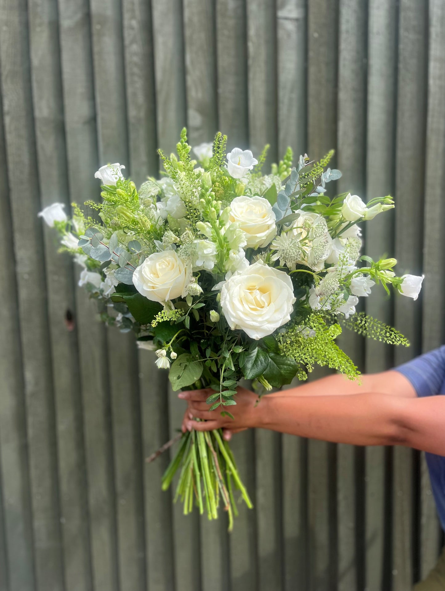 Bouquet of white and green flowers held by a person against a wooden fence.