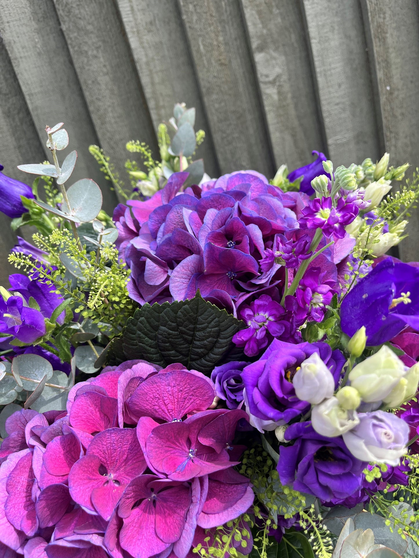 Bouquet of purple and pink flowers with greenery against a wooden fence.