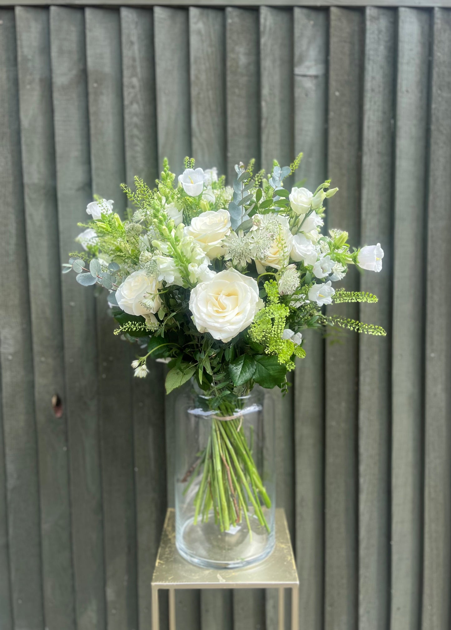 Bouquet of white and green flowers in a clear vase against a wooden background