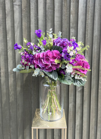 Bouquet of purple and pink flowers in a clear vase against a wooden background