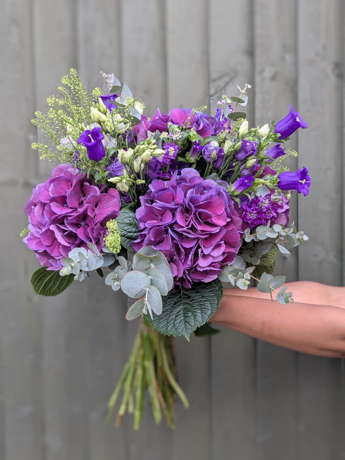 Bouquet of purple flowers held by a hand against a gray wooden background