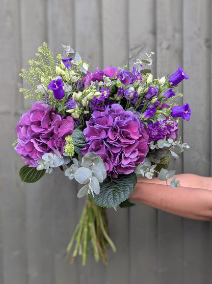 Bouquet of purple flowers held by a hand against a gray wooden background