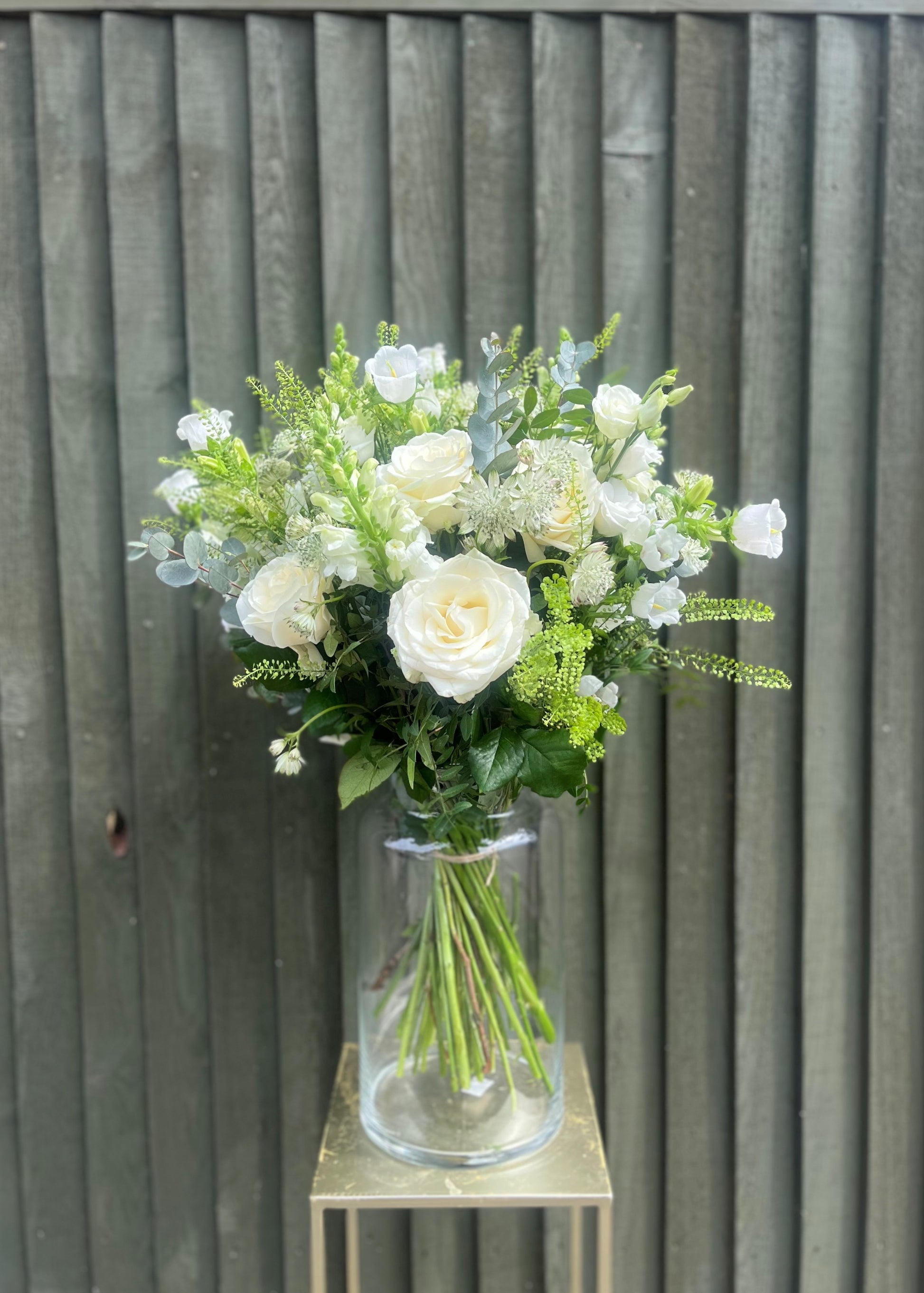 Bouquet of white and green flowers in a clear vase against a wooden background